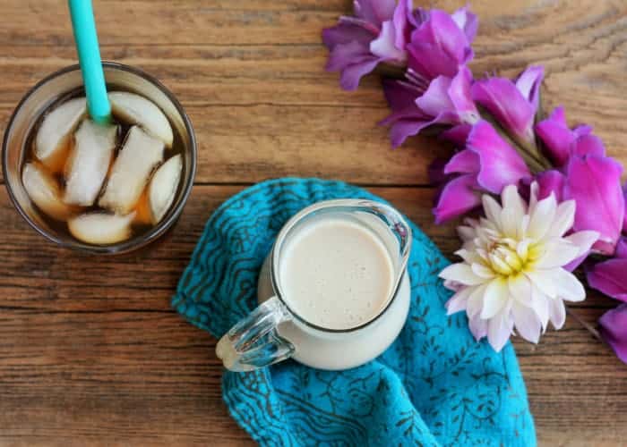 sugar-free coffee creamer in a pitcher on a blue cloth with flowers and iced coffee