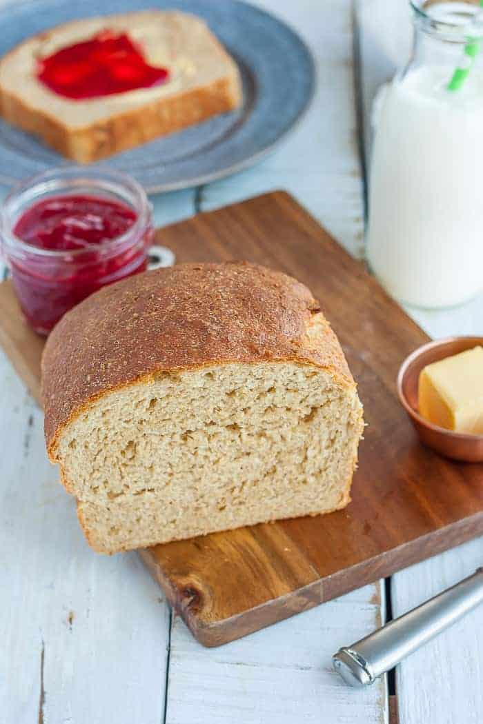 A loaf of honey wheat bread on a cutting board with a dish of jam