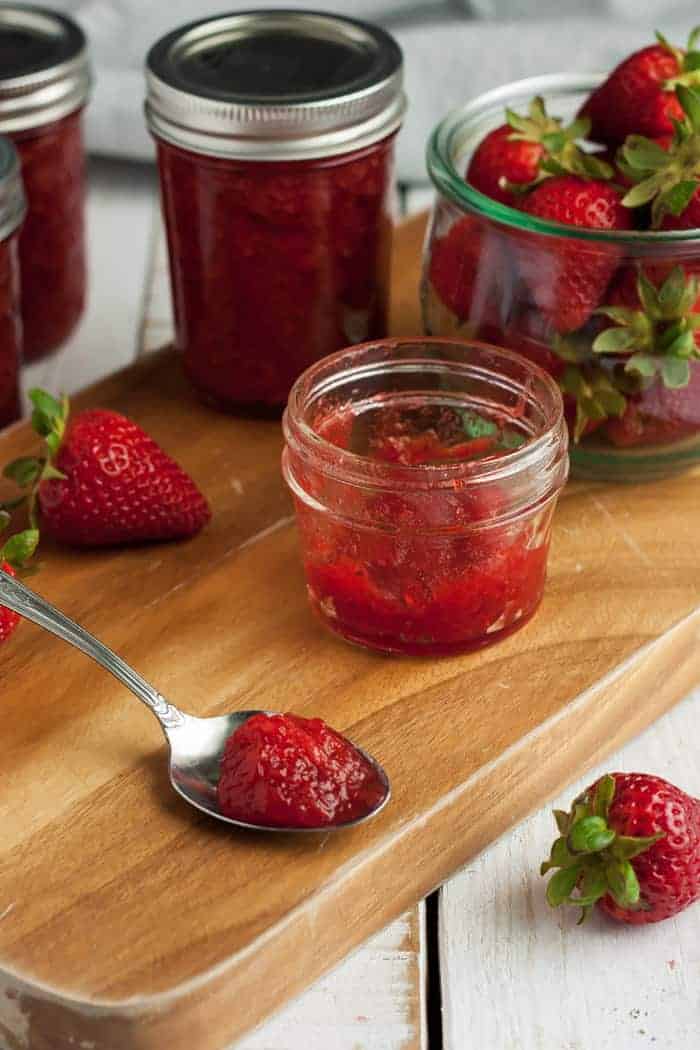 Four jars of low-sugar strawberry preserves on a wooden board