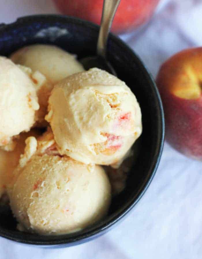 Three scoops of homemade peach ice cream in a blue bowl with a spoon