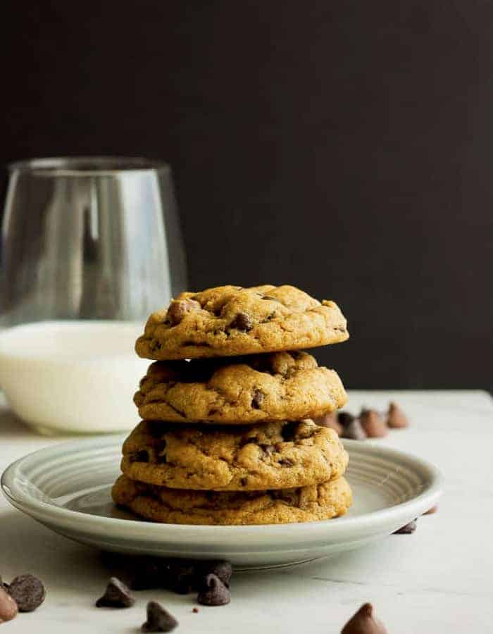 four whole wheat chocolate chip cookies on a plate with a glass of milk
