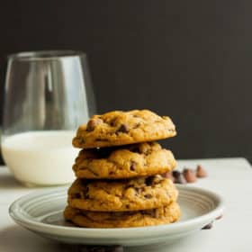 A stack of whole wheat chocolate chip cookies on a plate with a glass of milk