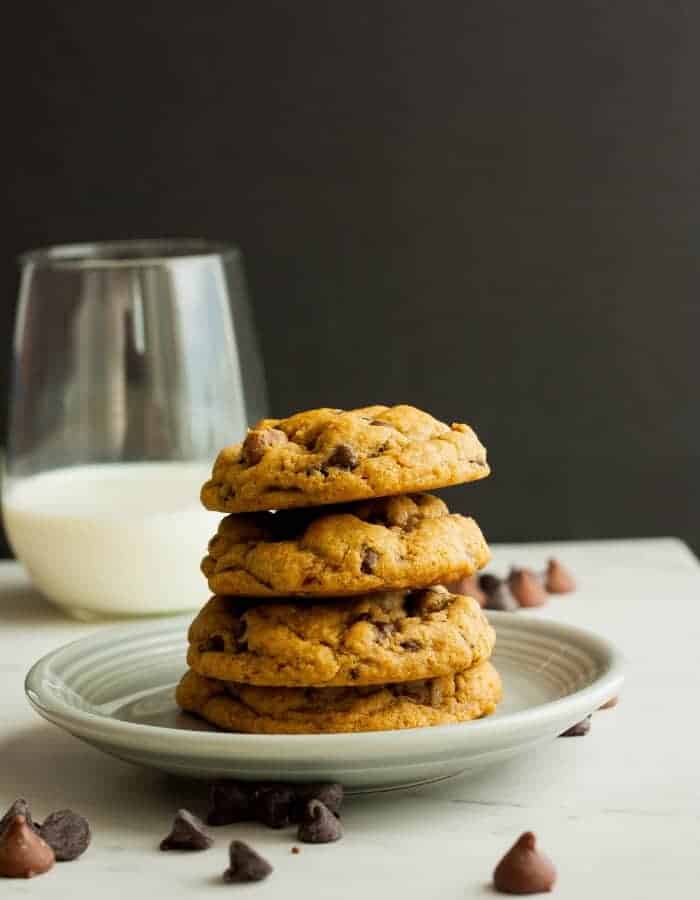 A stack of whole wheat chocolate chip cookies on a plate with a glass of milk