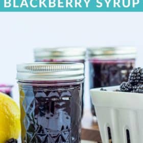 jars of blackberry syrup and a basket of blackberries on a white board
