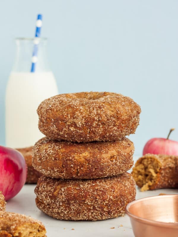 3 cinnamon apple donuts stacked up with apples and a bottle of milk