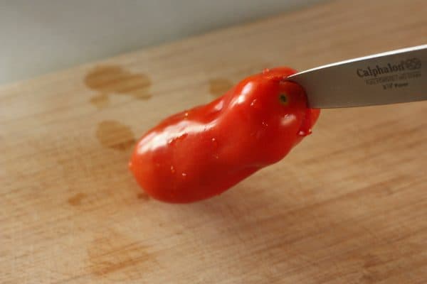 a knife cutting into a tomato to remove the core