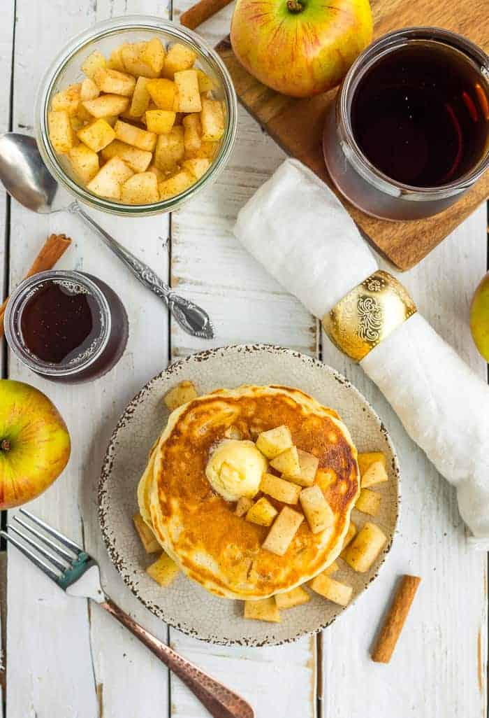 an overhead photo of apple pancakes on a plate with butter and diced apples