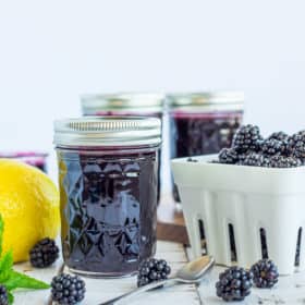 jars of blackberry syrup and a basket of blackberries on a white board