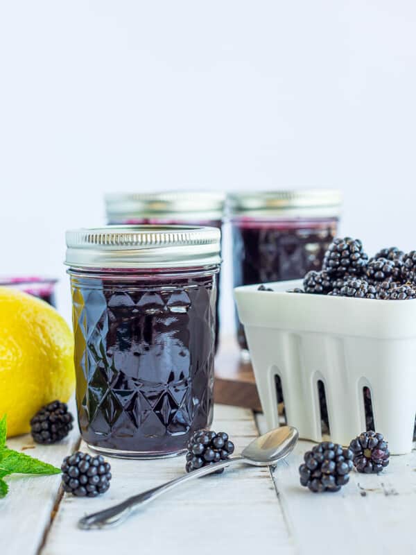 jars of blackberry syrup and a basket of blackberries on a white board