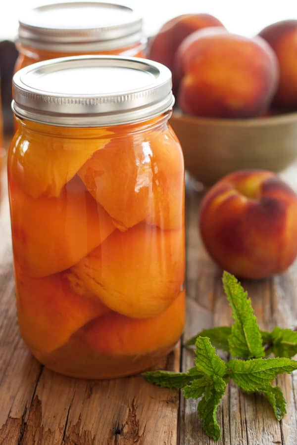 a jar of canned peaches with fresh peaches and mint
