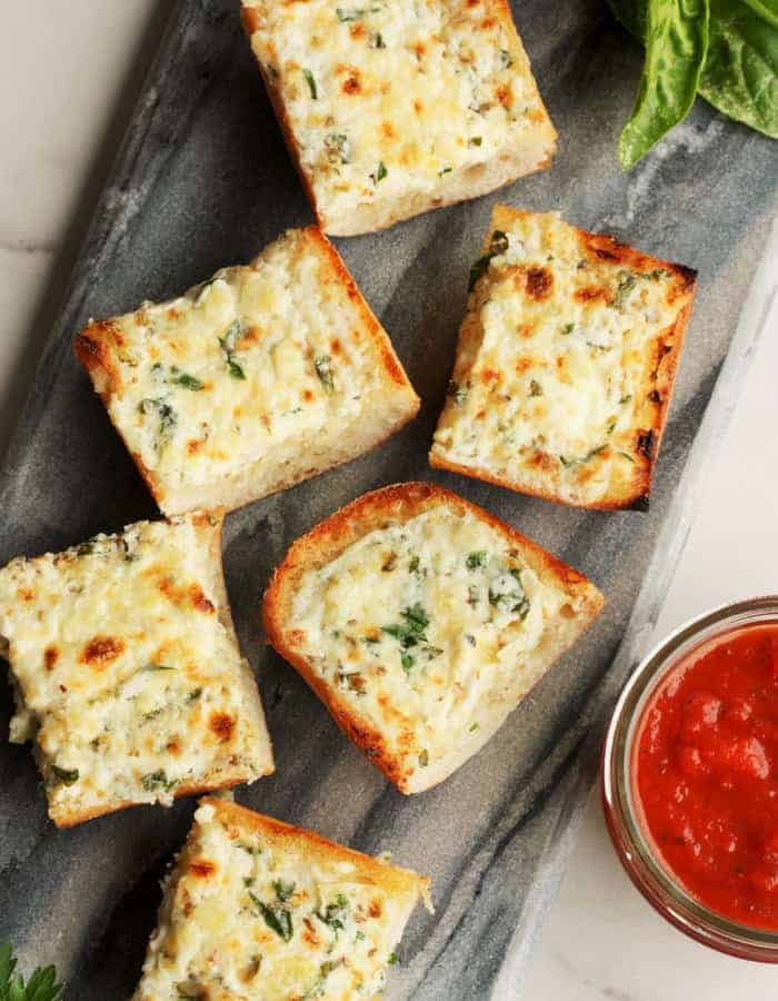 cheesy garlic bread with herbs and marinara sauce on a grey board