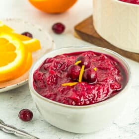 a bowl of orange cranberry sauce topped with fresh cranberries and orange zest