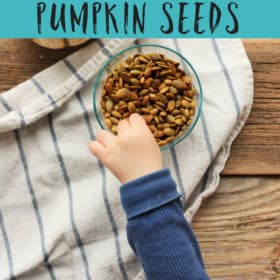 A toddler's hand grabbing a bowl of white cheddar salted pumpkin seeds