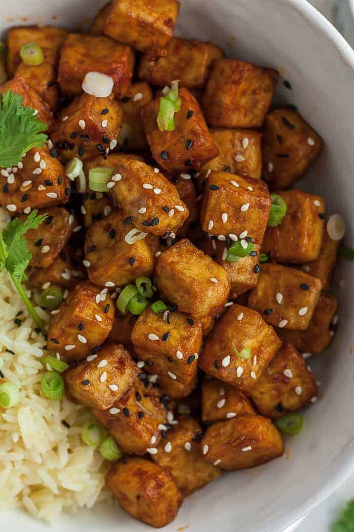 a bowl of crispy tofu with green onions, rice, and sesame seeds