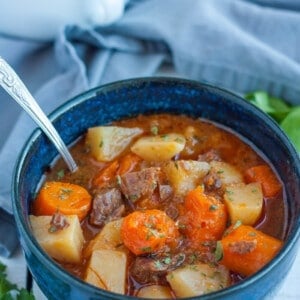 Instant pot beef stew in a blue bowl with a spoon and a grey cloth