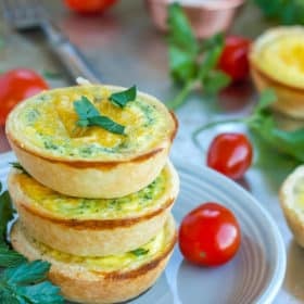 three mini quiche appetizers on a plate with tomatoes and herbs