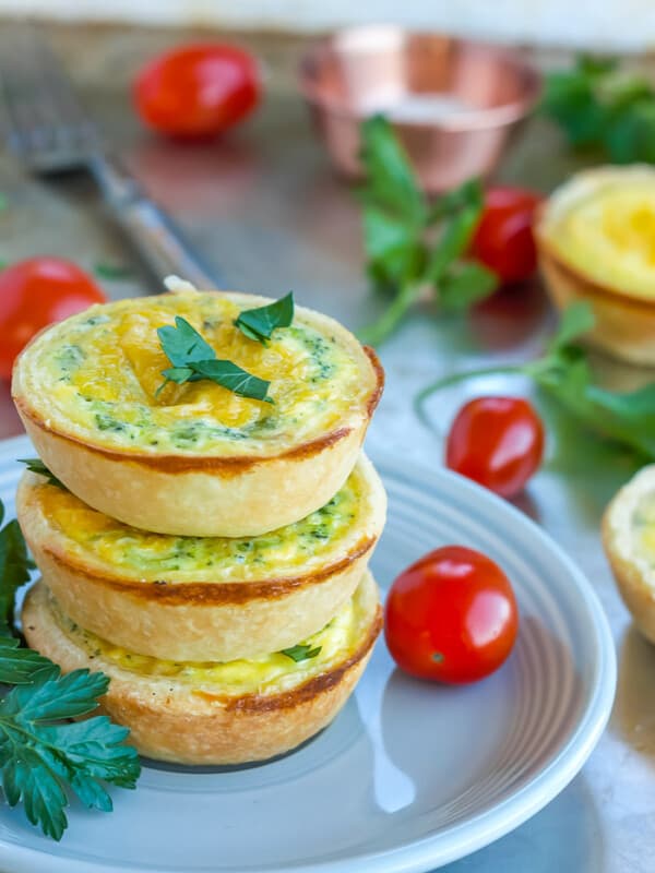 three mini quiche appetizers on a plate with tomatoes and herbs