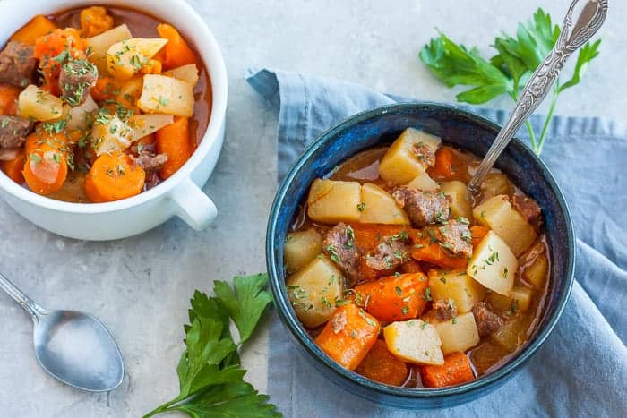 Two bowls of whole30 beef stew with fresh parsley on a white board