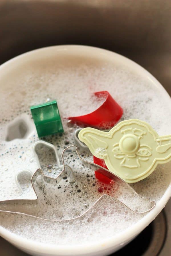 These are the best homemade Soft Whole Wheat Sugar Cookies ever! This easy recipe has a life-changing hack to make the dough so simple to roll out. #sustainablecooks #wholewheat #sugarcookies #christmascookies cookie cutters in a bowl of soapy water