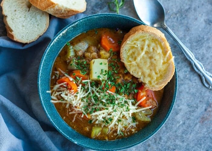 a blue bowl of instant pot lentil soup with cheese bread and a spoon