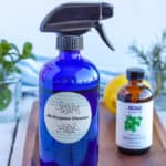 a bottle of homemade all-purpose cleaner on a wooden tray with essential oils, lemon, and fresh mint