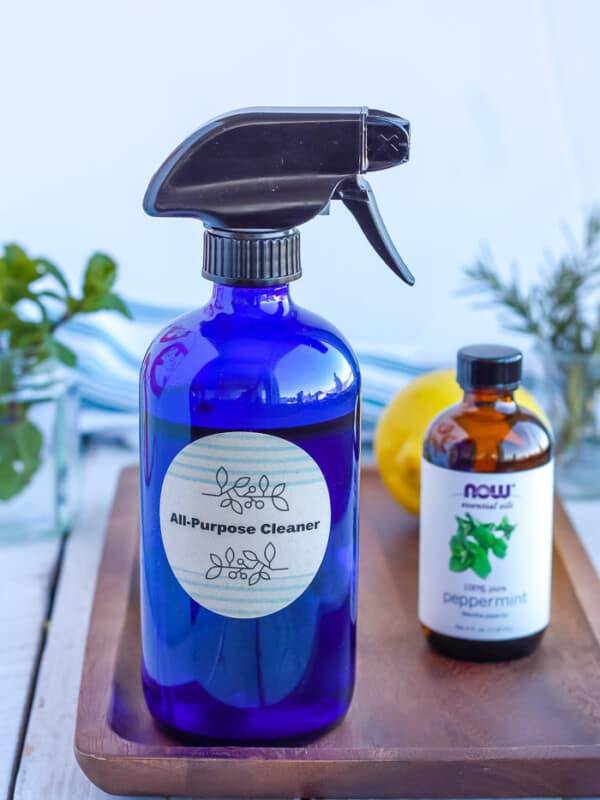 a bottle of homemade all-purpose cleaner on a wooden tray with essential oils, lemon, and fresh mint