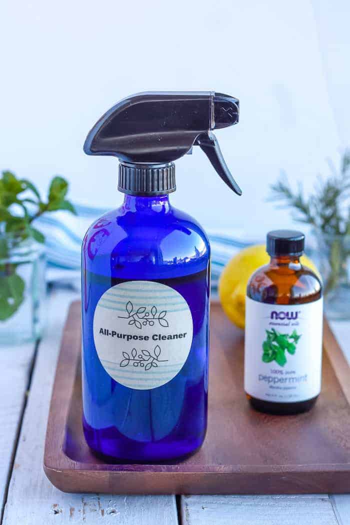 a bottle of homemade all-purpose cleaner on a wooden tray with essential oils, lemon, and fresh mint