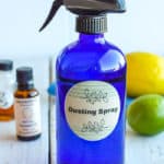 a blue bottle of homemade dusting spray with essential oils and a lemon and lime