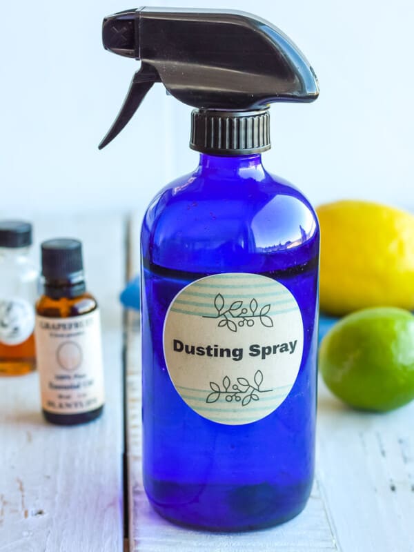 a blue bottle of homemade dusting spray with essential oils and a lemon and lime