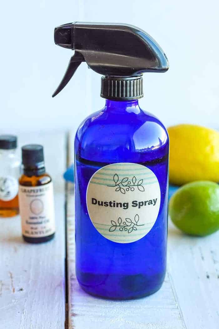 a blue bottle of homemade dusting spray with essential oils and a lemon and lime