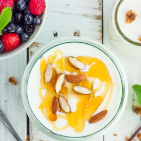 A glass dish of yogurt topped with honey and almonds