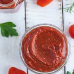 a jar of sugar-free pizza sauce on a white board with tomatoes and herbs