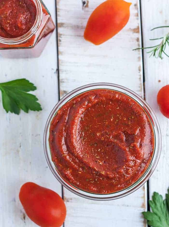 a jar of sugar-free pizza sauce on a white board with tomatoes and herbs