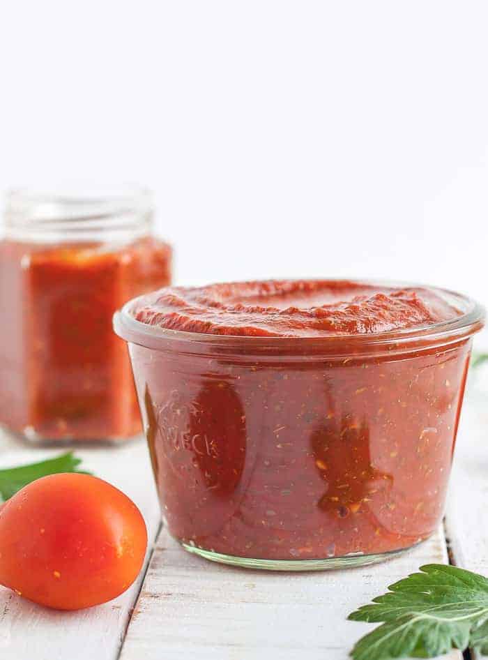 2 jars of homemade pizza sauce with tomatoes and herbs on a white board