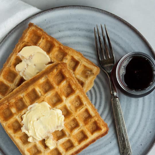 whole grain waffles on a grey plate with a fork and syrup