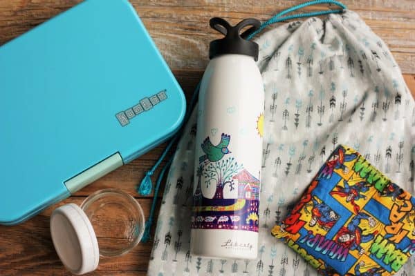 A yumbox lunchbox, liberty bottlesworks waterbottle, and mason jar on a wooden background