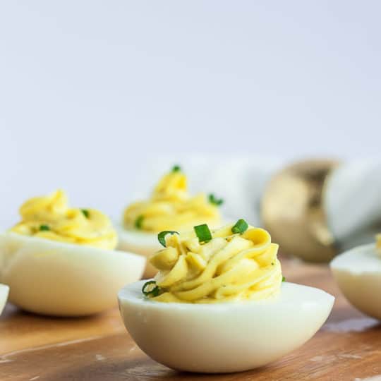 A side view of healthy deviled eggs topped with chives on a wooden cutting board
