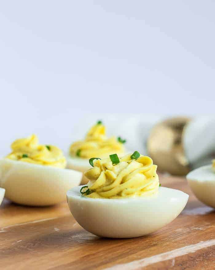 A side view of healthy deviled eggs topped with chives on a wooden cutting board