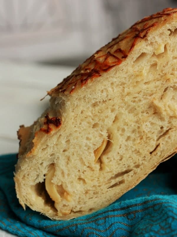 a slice of roasted garlic and Asiago cheese no knead bread on a teal cloth