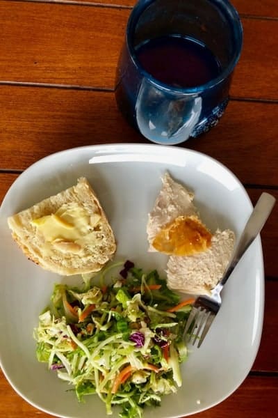 bread with butter, roasted chicken, and salad on a plate with a glass of water on a table