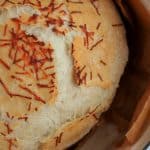 a loaf of no knead bread topped with asiago cheese in a teal dutch oven
