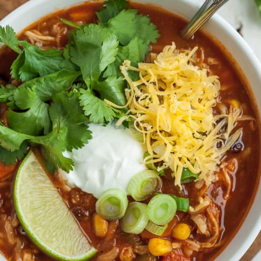 Instant Pot tortilla soup in a bowl with cilantro, sour cream, cheese, lime, and green onion