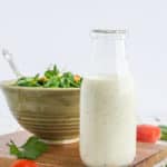 A glass bottle of ranch dressing in front of a bowl of salad