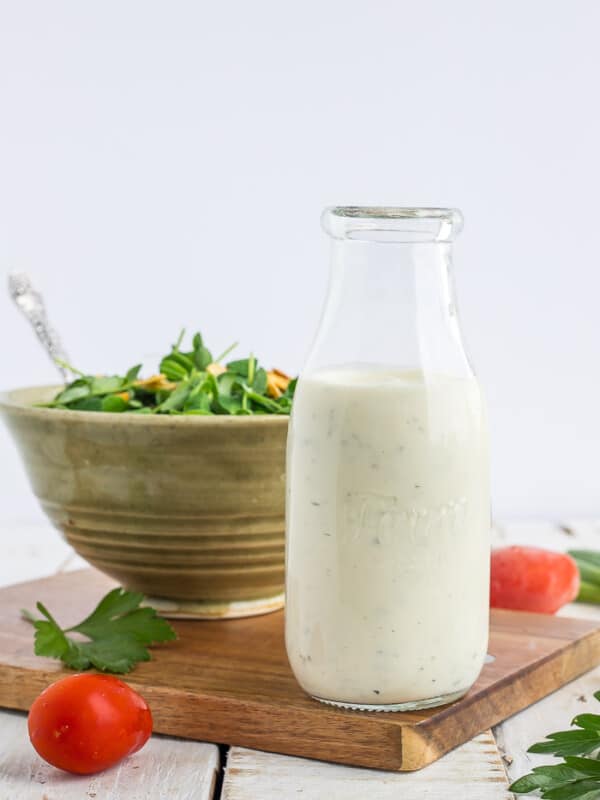 A glass bottle of ranch dressing in front of a bowl of salad