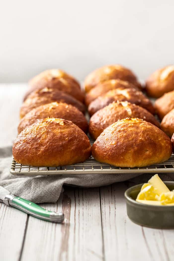 homemade pretzel buns cooling on a rack with a dish of butter
