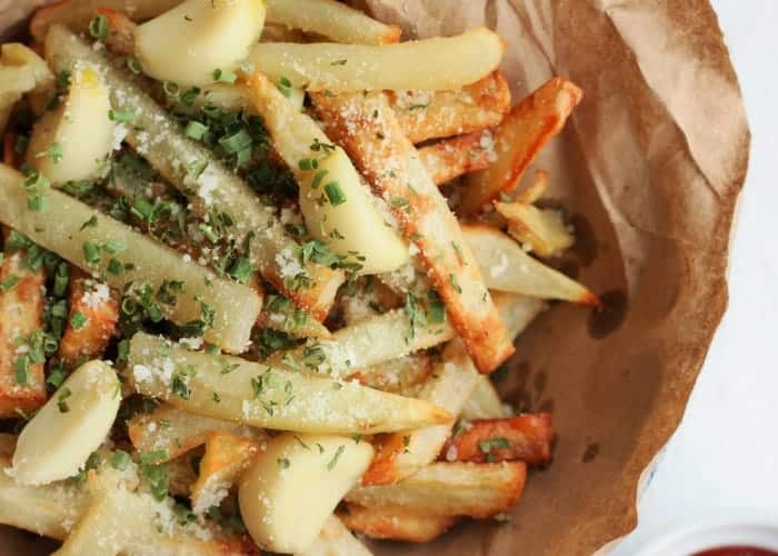 homemade air fry french fries in a bowl with brown paper. Topped with parsley, roasted garlic and parmesan cheese