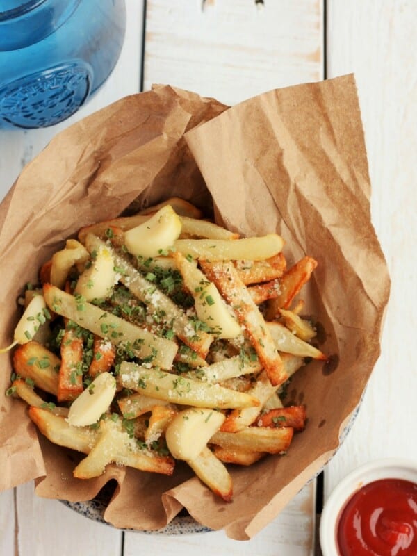 air fryer french fries in a bowl with brown paper, ketchup, and a blue glass on a white background