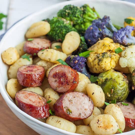 A white bowl full of fried gnocchi, chicken sausage, and roasted veggies
