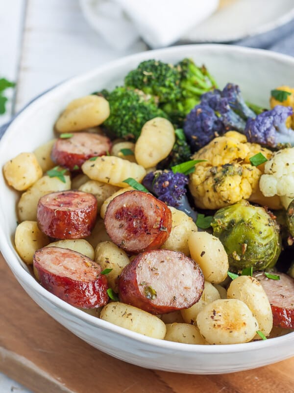 A white bowl full of fried gnocchi, chicken sausage, and roasted veggies