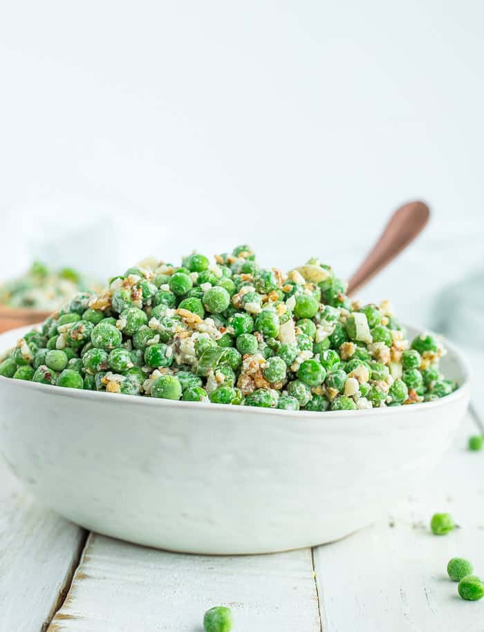a white bowl with healthy green pea salad and a bronze spoon